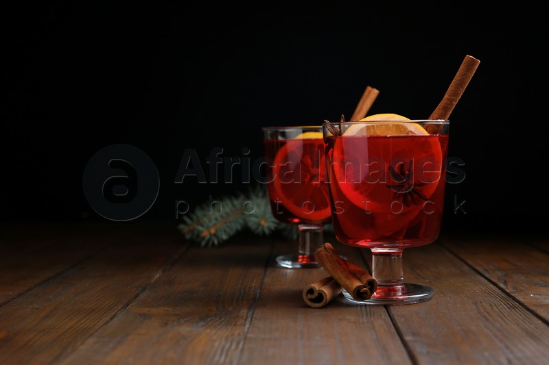 Glasses with red mulled wine on wooden table against dark background. Space for text