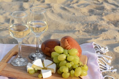 Glasses with white wine and snacks for beach picnic on sand outdoors