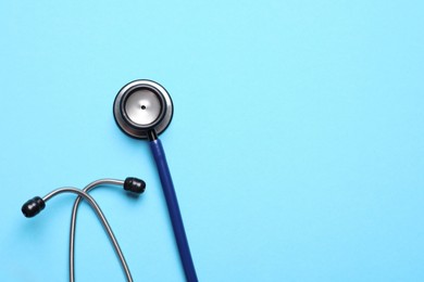 Stethoscope on light blue background, top view. Space for text