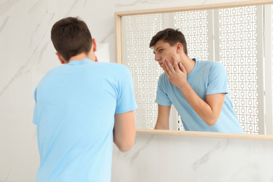 Teen guy with acne problem near mirror in bathroom