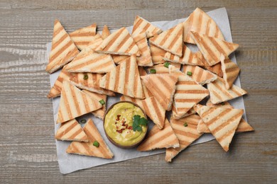 Delicious pita chips and hummus on wooden table, top view
