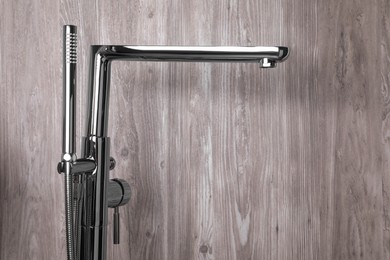 Modern bathtub faucet with hand shower on wooden background. Space for text