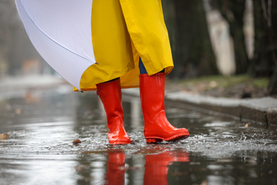 Woman in rubber boots with umbrella walking outdoors on rainy day, closeup