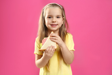 Photo of Cute little girl with tasty sandwich on pink background