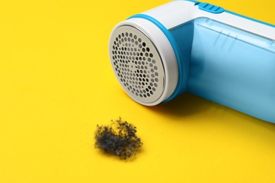 Photo of Modern fabric shaver and lint on yellow background, closeup