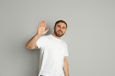 Happy young man waving to say hello on light grey background