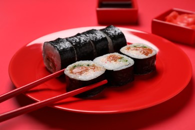 Tasty sushi rolls and chopsticks on red background, closeup