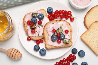 Tasty sandwiches with cream cheese, berries and honey on white table, flat lay