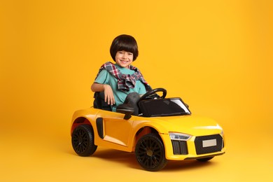 Little child driving toy car on yellow background