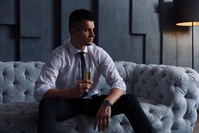 Photo of Handsome businessman with glass of champagne on sofa indoors. Luxury lifestyle