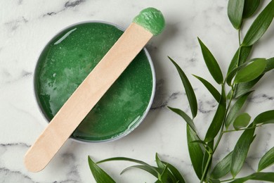 Photo of Spatula with wax and leaves on white marble table, flat lay