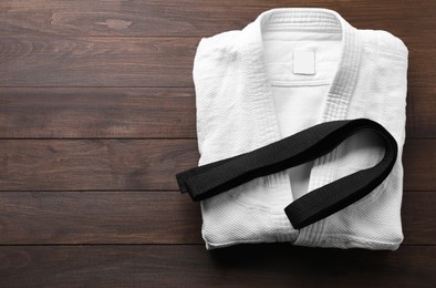 Martial arts uniform and black belt on wooden background, top view. Space for text