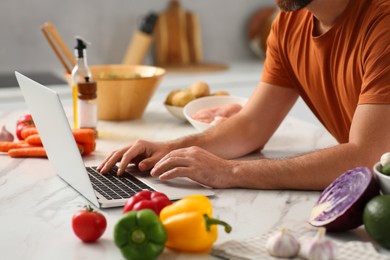 Photo of Man making dinner while watching online cooking course via laptop in kitchen, closeup
