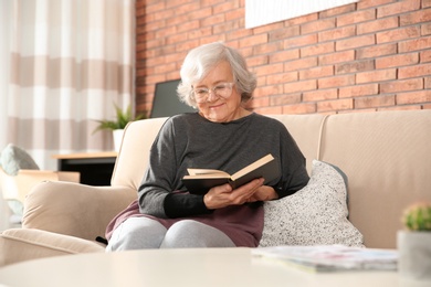 Elderly woman reading book on sofa in living room