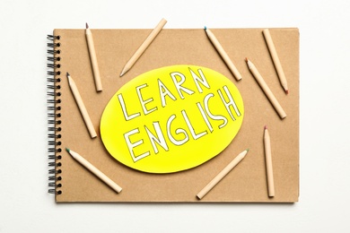 Notepad with phrase Learn English and pencils on white background, top view