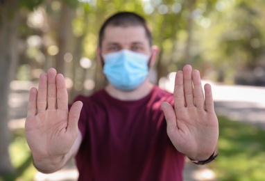 Man in protective face mask showing stop gesture outdoors, focus on hands. Prevent spreading of coronavirus