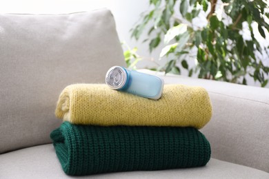 Photo of Modern fabric shaver and woolen sweaters on sofa indoors