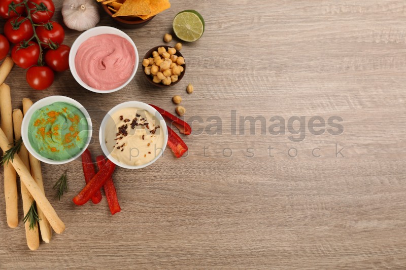 Different kinds of tasty hummus served with bread sticks on wooden table, flat lay. Space for text