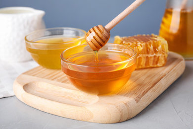 Photo of Dripping tasty aromatic honey from dipper into bowl on light grey table