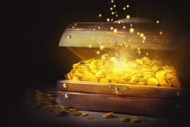 Image of Open treasure chest with gold coins on wooden table against black background