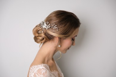 Young bride with elegant wedding hairstyle on light grey background