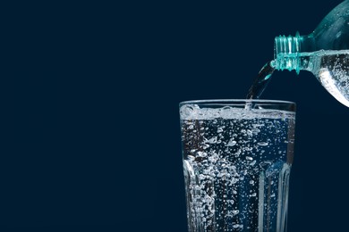 Pouring soda water from bottle into glass on blue background, closeup. Space for text