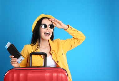 Beautiful woman with suitcase and ticket in passport for summer trip on blue background. Vacation travel