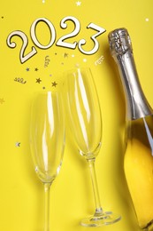 Happy New Year 2023! Flat lay composition with bottle of sparkling wine on yellow background