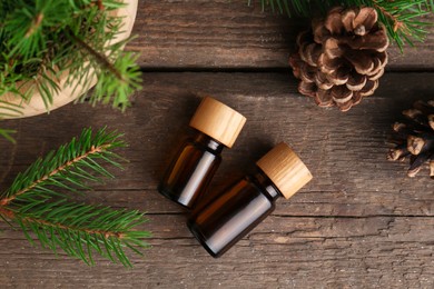 Bottles of pine essential oil, conifer tree branches and cones on wooden table, flat lay