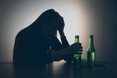 Alcohol addiction. Silhouette of woman holding beer bottle at table, backlit