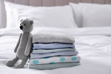 Stack of clean baby's clothes and toy on bed