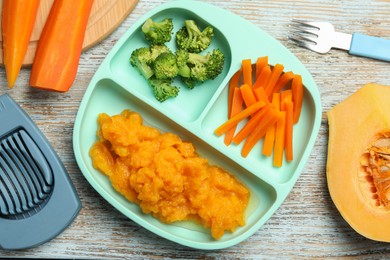 Photo of Baby food. Section plate with vegetables and pumpkin puree served on rustic wooden table, flat lay