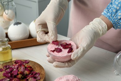 Woman putting flower petals in bath bomb mold at white table indoors, closeup