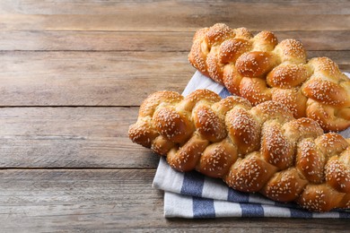 Homemade braided breads with sesame seeds on wooden table, space for text. Traditional Shabbat challah