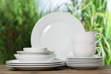Photo of Set of clean dishware on wooden table against blurred background