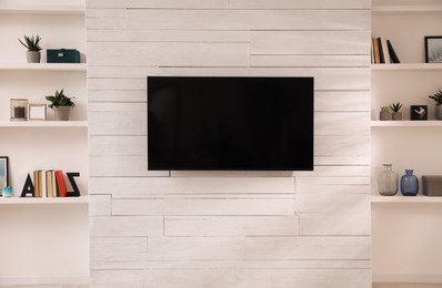 Tv set mounted on wall between niches with shelves in room. Interior design