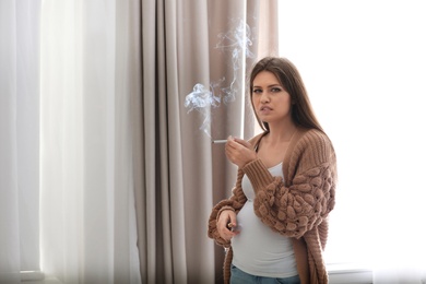 Young pregnant woman smoking cigarette at home. Harm to unborn baby