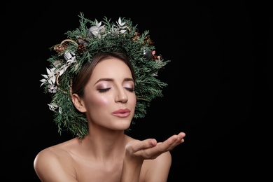 Photo of Beautiful young woman with Christmas wreath blowing kiss on black background. Space for text
