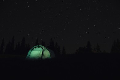 Camping tent glowing at night outdoors. Space for text
