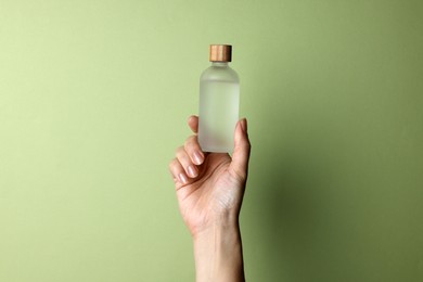 Woman holding bottle of cosmetic product on pale olive background, closeup. Space for text