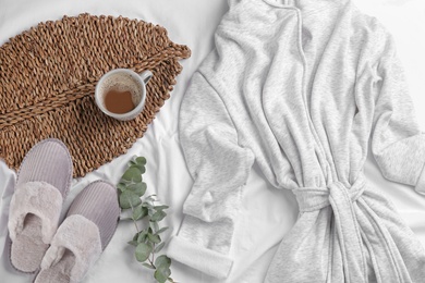 Flat lay composition with slippers and bath robe on white bedsheet. Comfortable home outfit
