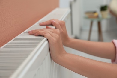 Woman warming hands on heating radiator indoors, closeup