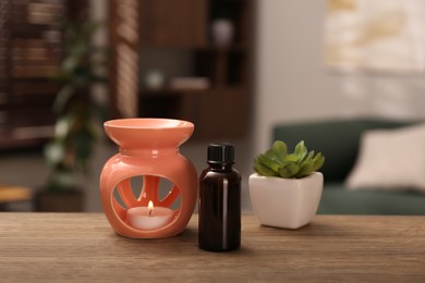 Aroma lamp with small candle, bottle of oil and houseplant on wooden table indoors