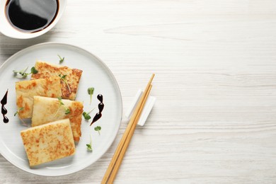 Delicious turnip cake and soy sauce served on white wooden table, flat lay. Space for text
