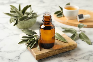 Bottle of essential sage oil and leaves on white marble table
