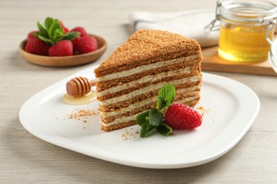 Photo of Slice of delicious layered honey cake with mint and raspberry on wooden table