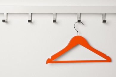 Rack with empty orange clothes hanger on white wall
