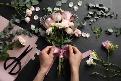 Florist creating beautiful bouquet at black table, top view
