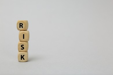 Stack of wooden cubes with word Risk on light grey background. Space for text