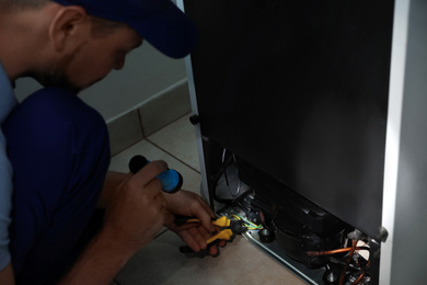 Electrician with flashlight fixing refrigerator indoors, closeup